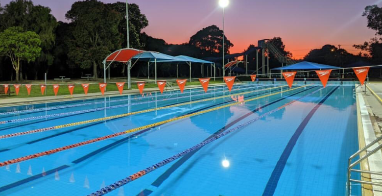 Photo of the 50m pool early in the morning with the sun rising in the background.