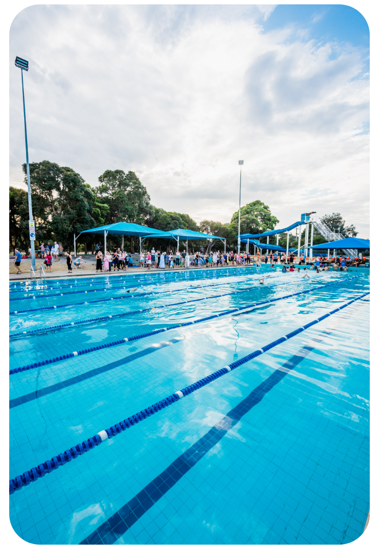 Photo of the 50m pool at Pines, with people in the background and the waterslide.